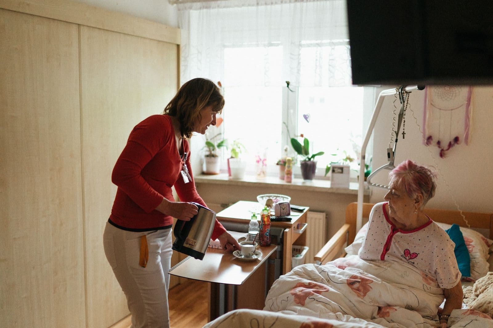 A carer sitting with an older woman in her own bedroom, talking together